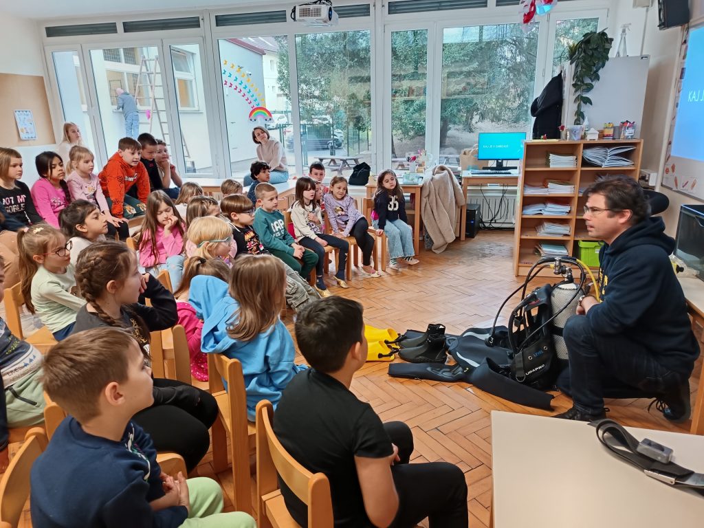 fotografiji so učenci prvega razreda in potapljač, ki predstavlja svoje delo